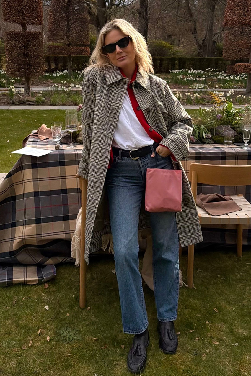 A woman wearing a plaid trench coat, white t-shirt, and blue jeans.