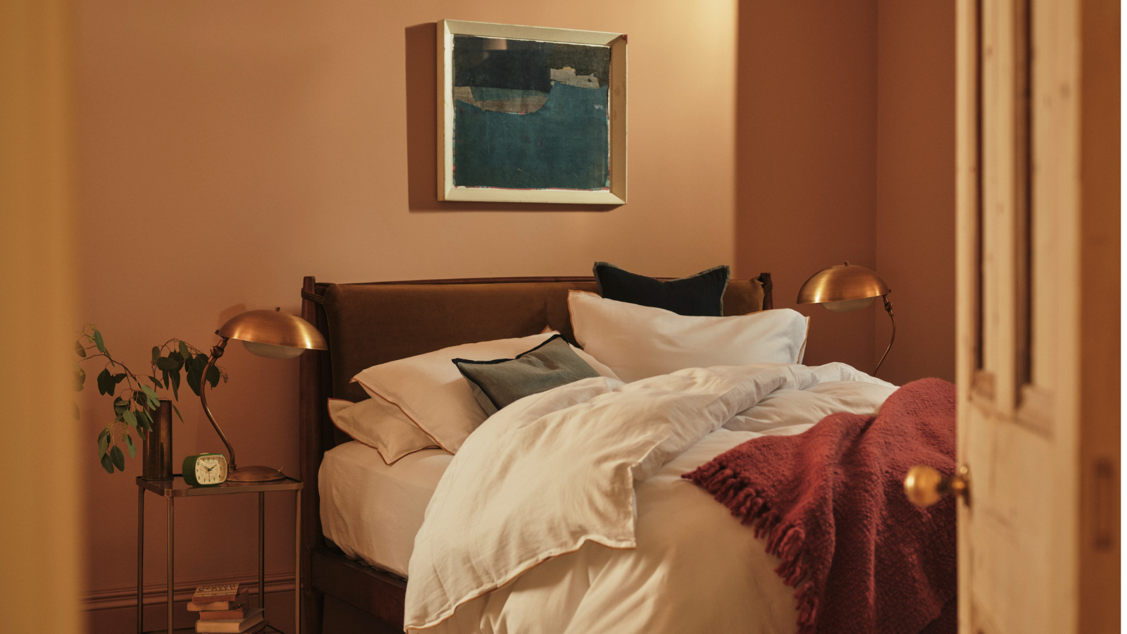 Bedroom with peach walls, two bedside tables with gold lamps and white duvet bed in middle