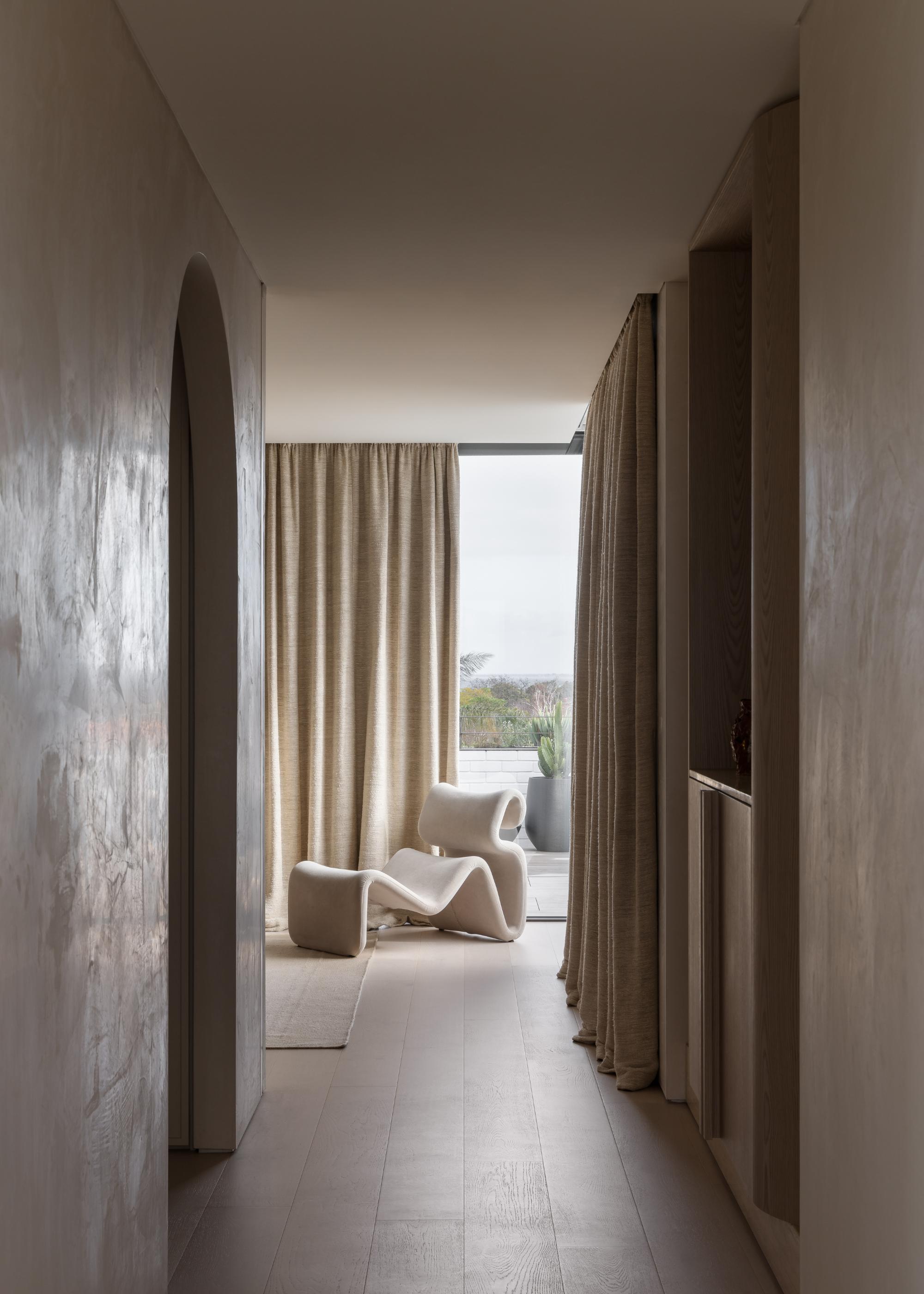 A long hallway leading to a bedroom with a cream 'etcetera' lounge chair