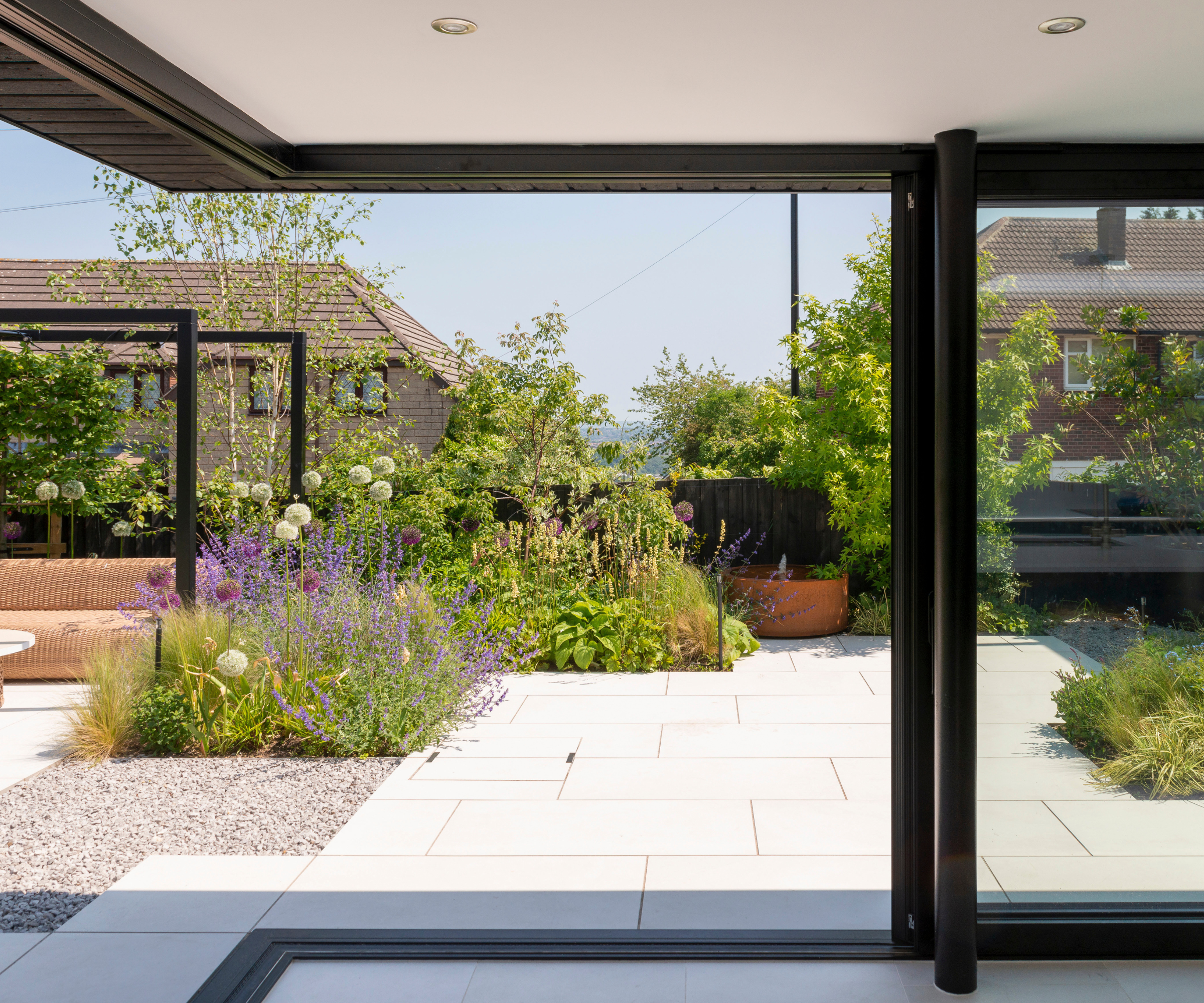 The garden from the kitchen patio doors, revealing a white patio, flower beds, and a pergola seating area just in view on the left hand corner