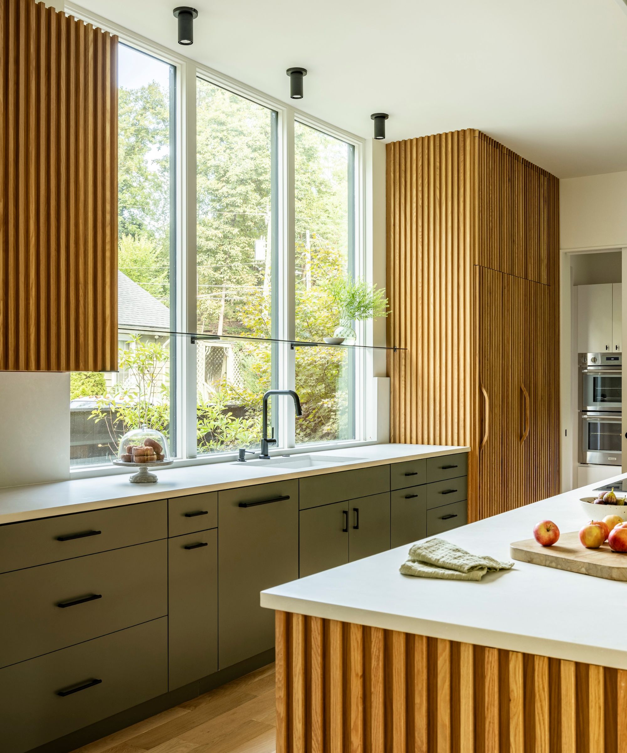 A wood and green kitchen featuring slated panels on the island and tall cabinets