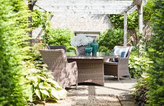 A rattan dining set in a leafy green courtyard