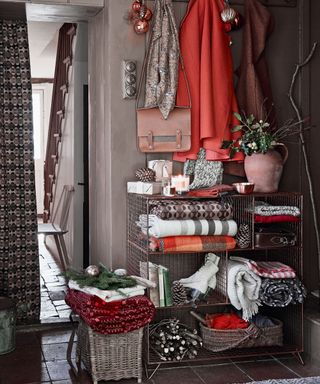 a mauve hallway with a selection of coats including a bright orange coat hanging up, with a wire storage unit underneath containing winter wooly blankets