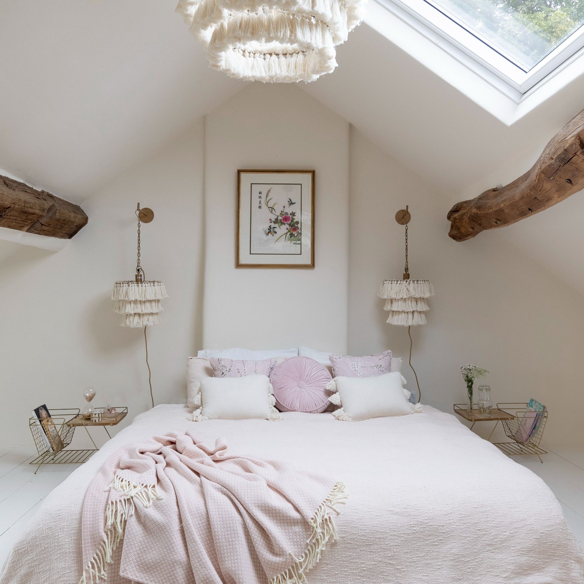 A bedroom with a bed with light pink sheets and a skylight
