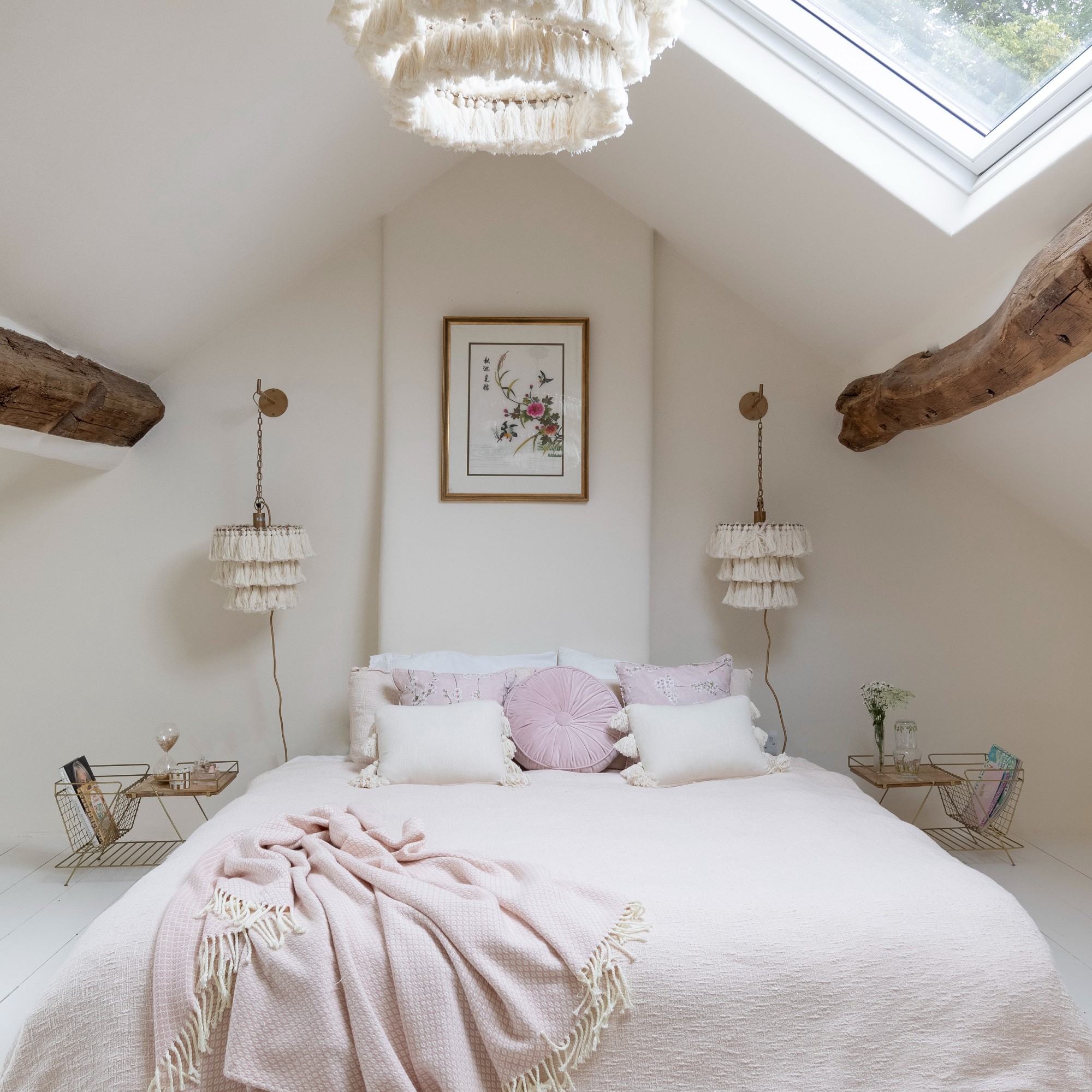 A bedroom with a bed with light pink sheets and a skylight