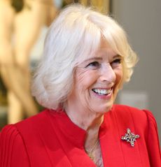 Queen Camilla wearing a red dress and diamond brooch smiling