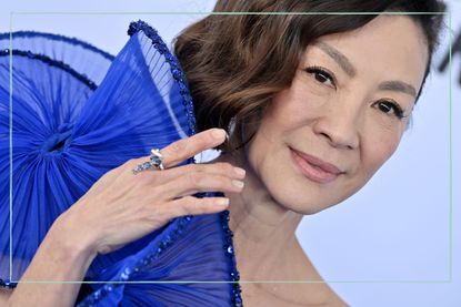 an extreme close up of Michelle Yeoh smiling at the camera in a purple dress