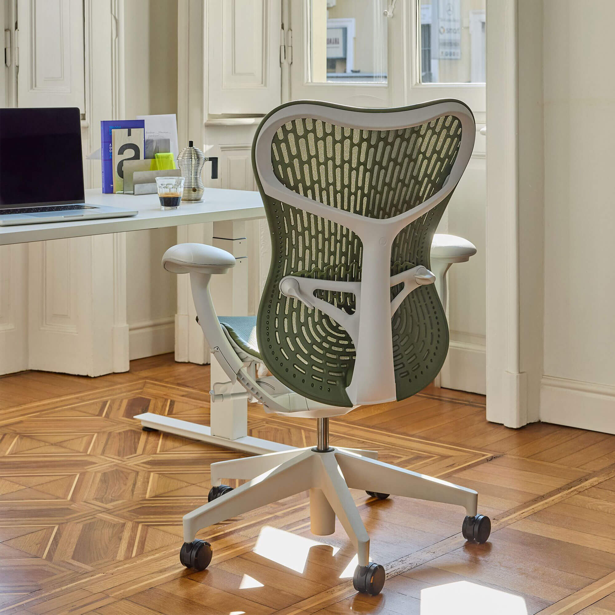 Light green-grey and white office chair on wooden floor at white desk with round white pendant light overhead