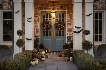 Charming entryway decorated for Halloween with wicker bat wall hangings, scattered pumpkins, and gothic wreaths