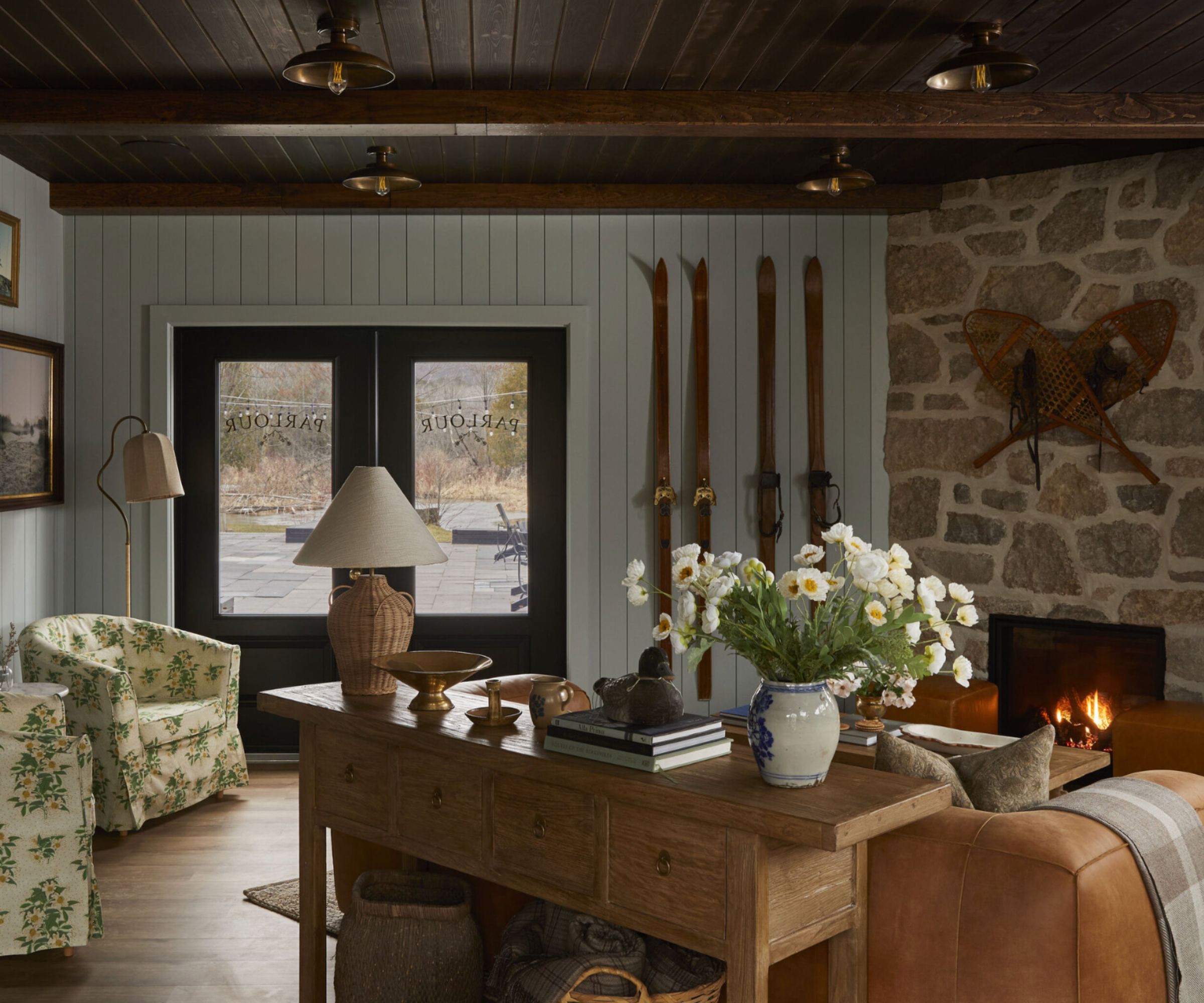 Cozy entryway with brick and panelled wood wall, gallery wall, two patterned armchairs, wooden console table decorated with ornaments, firepplace