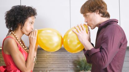 A man and a woman blow up balloons.