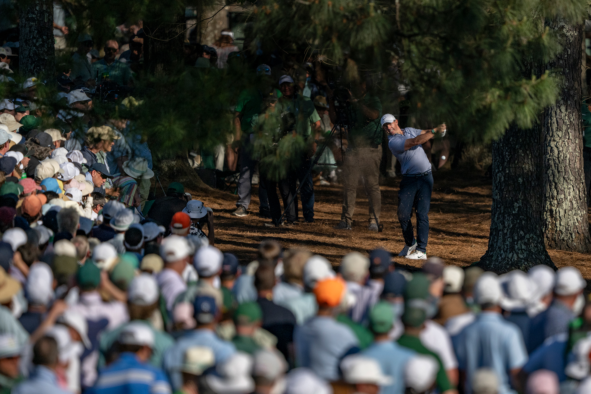 Rory McIlroy hitting a shot out of the trees at Augusta National, over the patrons heads who are lining the fairways