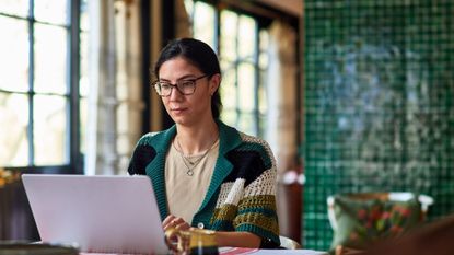 Woman in her 30's working from home sitting at table in dining room using laptop, home office, concentration, connection, working from home