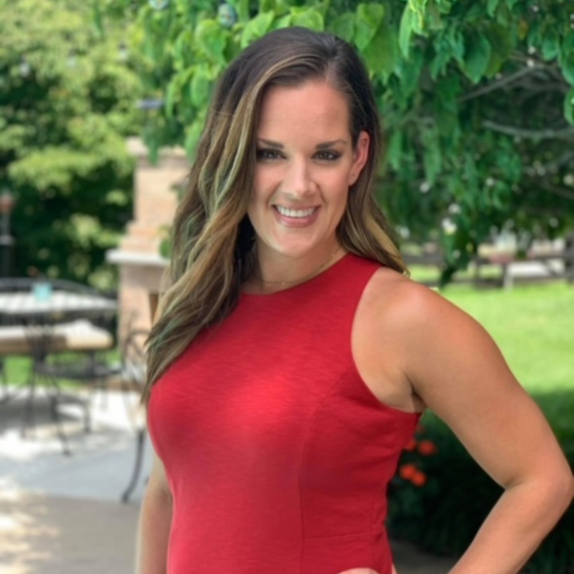 A picture of Katie Zimmerman, a woman with brown hair wearing a red dress stood outdoors