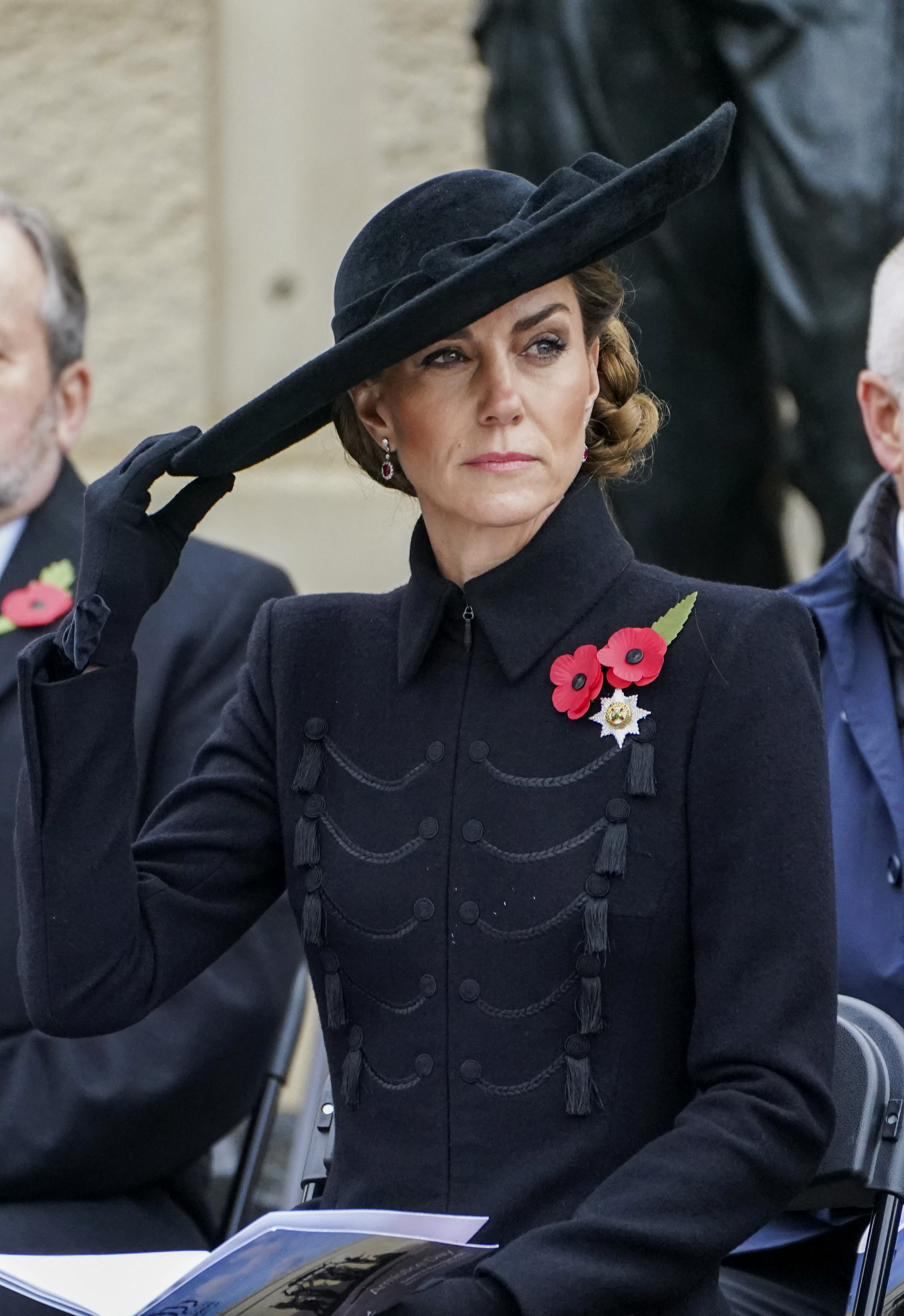 Kate Middleton wearing a black coat and h at sitting in a chair