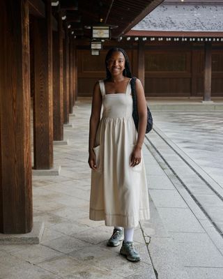 @taffymsipa wears an ivory linen midi dress with Salomon trainers.
