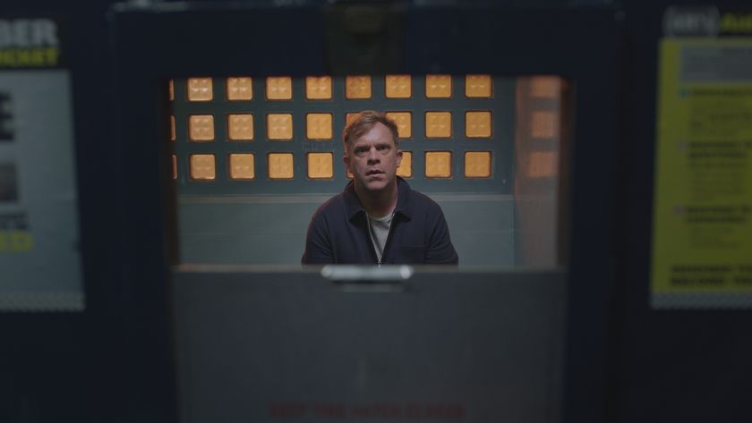 Dylan Keogh in a police cell looking out through the door slot in front of a grilled window backdrop. 