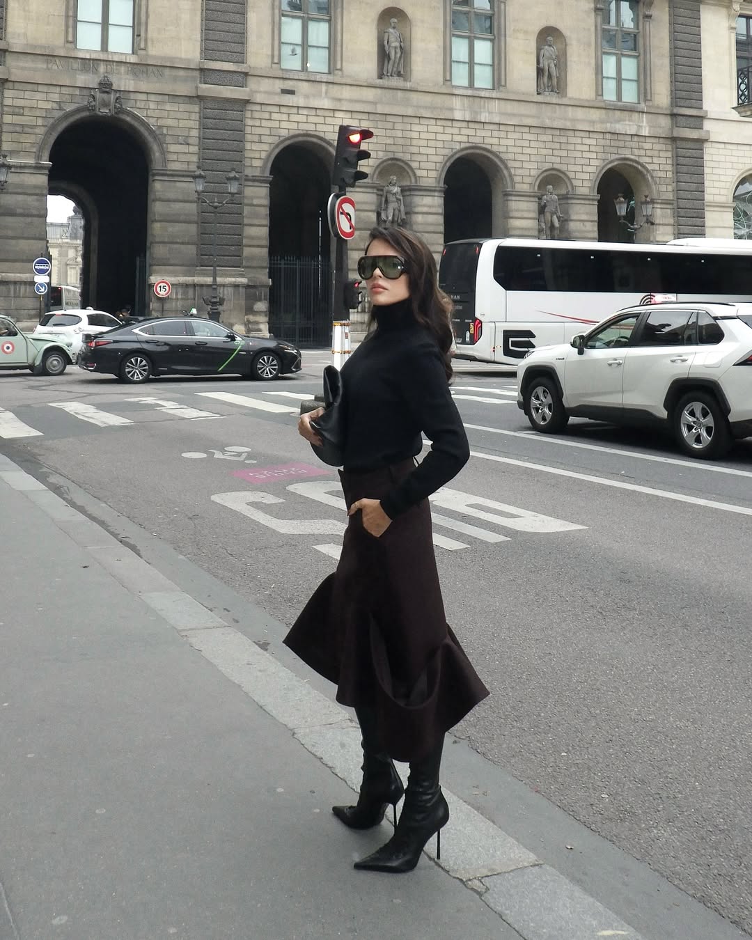 A woman wears a black sweater with a flared skirt and black stiletto boots.