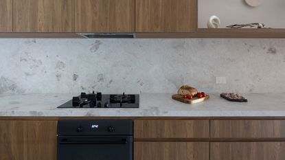 A timeless kitchen with wooden features as well as a gas stove and oven. On top of the marble countertop is a wooden board with bread on top 