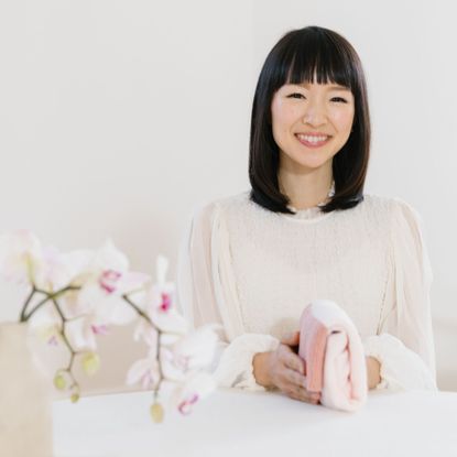Tidying guru Marie Kondo wears a white dress and smiles at the camera, next to a white and pink orchid