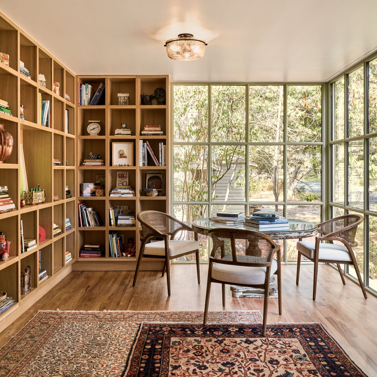dining room with bookshelf wrapping two walls, steel-framed windows, with a round dining table, two layered rugs, and four armchairs
