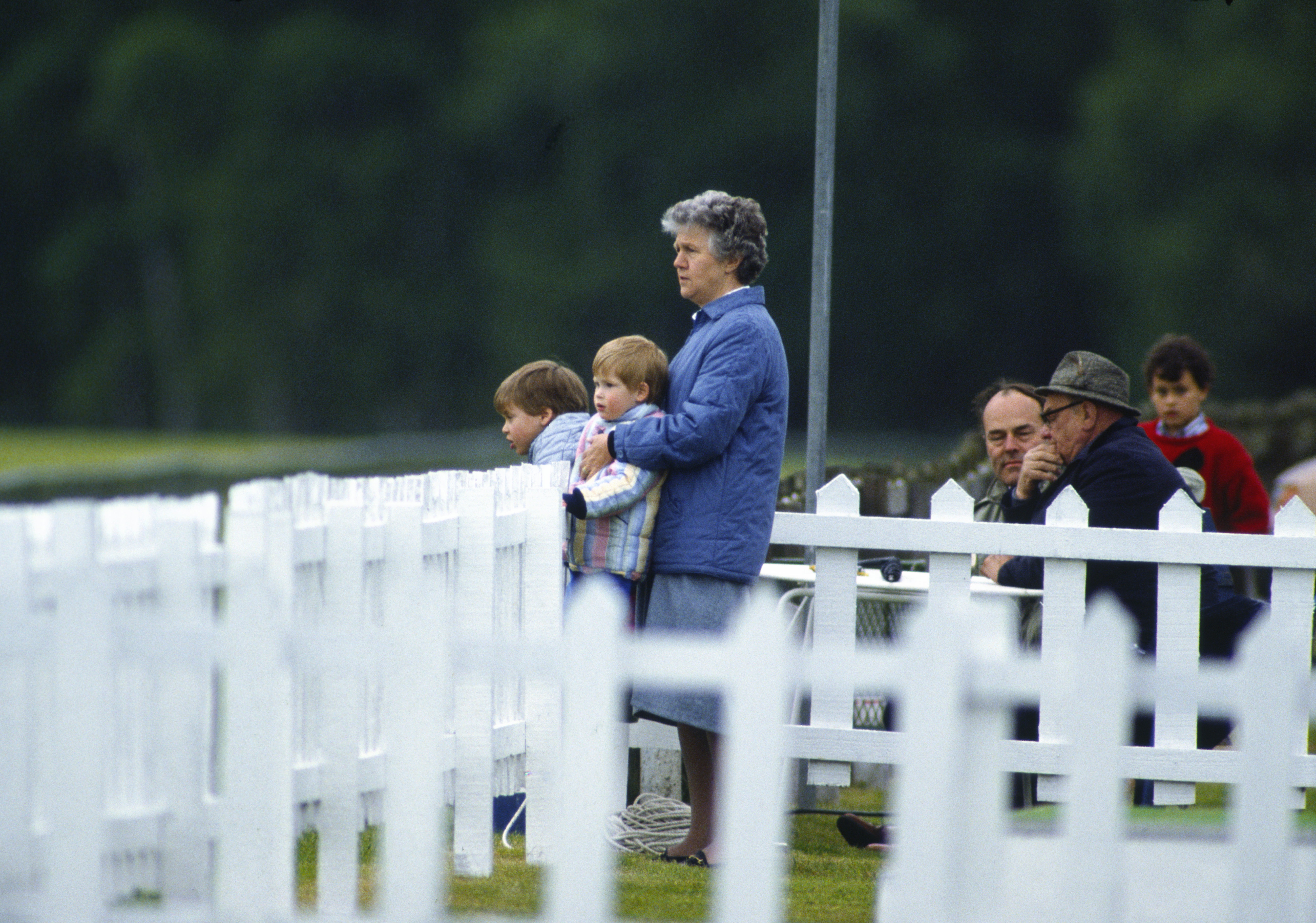 Prince Harry and William with their nanny watching polo behind a white fence
