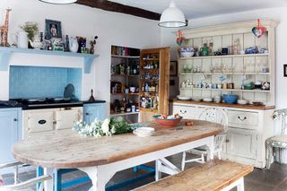 freestanding kitchen in a restored Georgian farmhouse, with a white dresser to the right, a large wooden dining table, a white aga within a blue tiled installed unit, and a wooden larder built into the wall