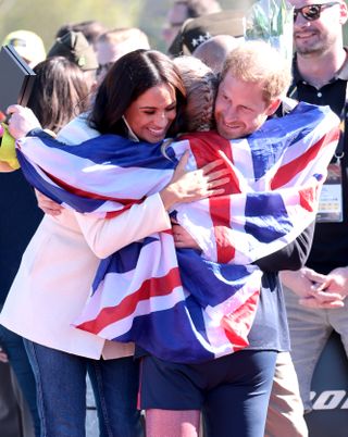 Meghan Markle and Prince Harry hug an Invictus games athlete wearing a British flag