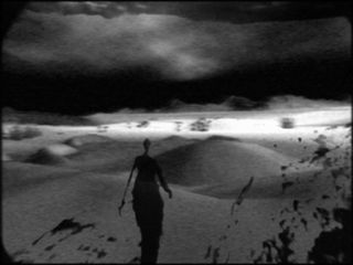 A slender black figure walking through the desert
