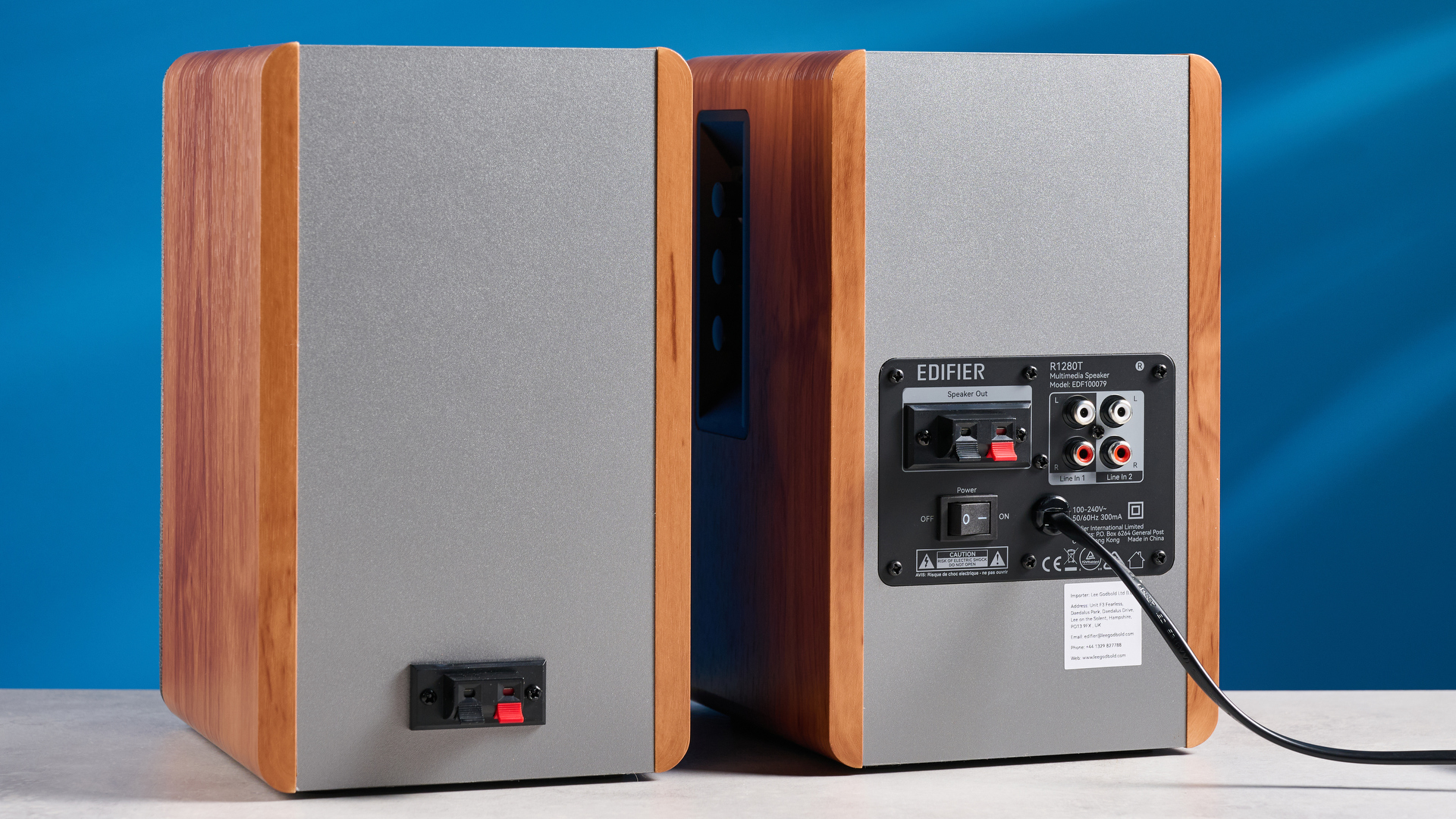 the edifier r1280t bookshelf speakers in wood brown photographed against the blue background, showing the volume adjustment dials, internal drivers and tweeters, RCA and aux inputs, and remote