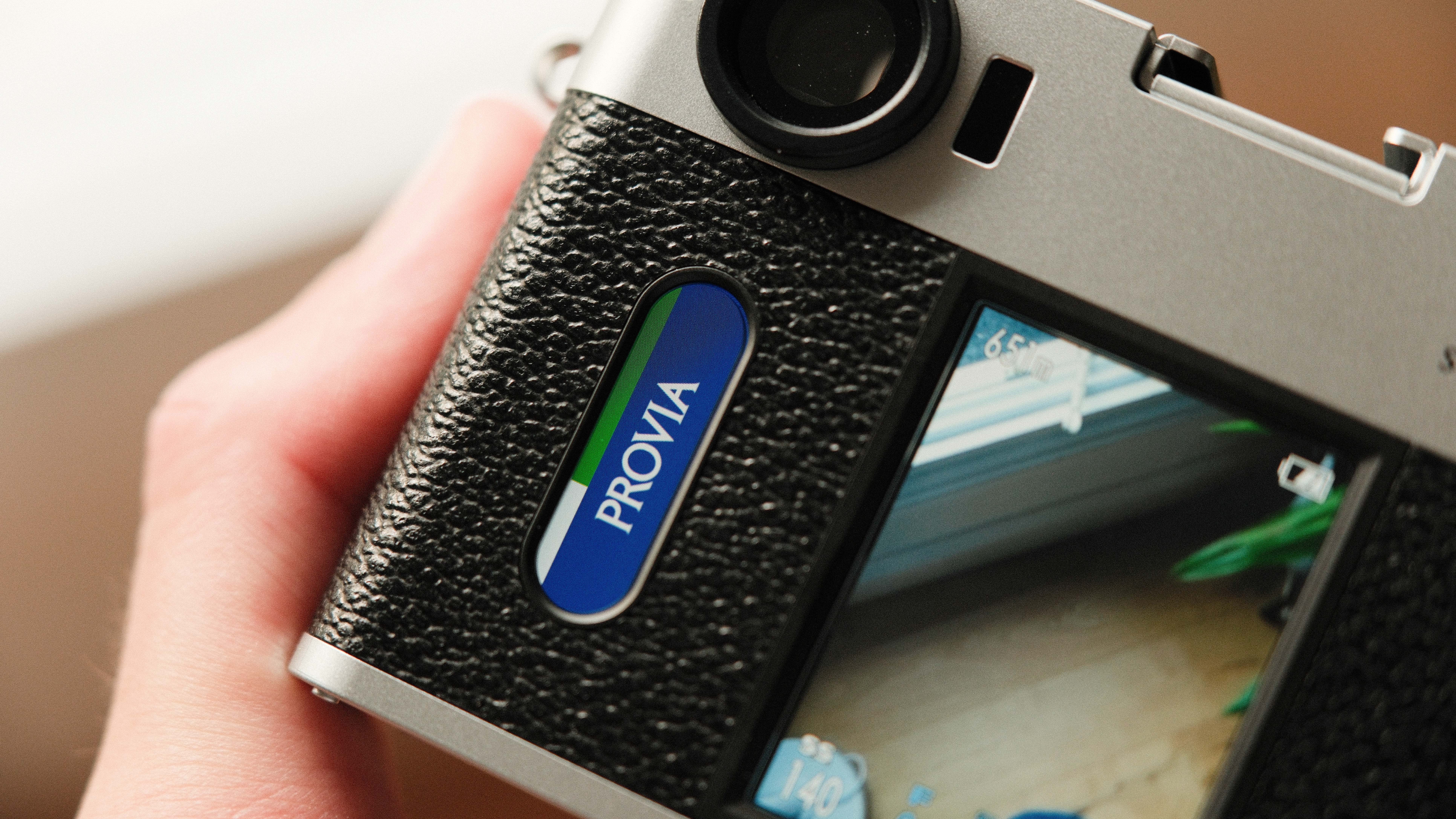 Fujifilm X Half camera held in a hand showing the film simulation window reading Provia
