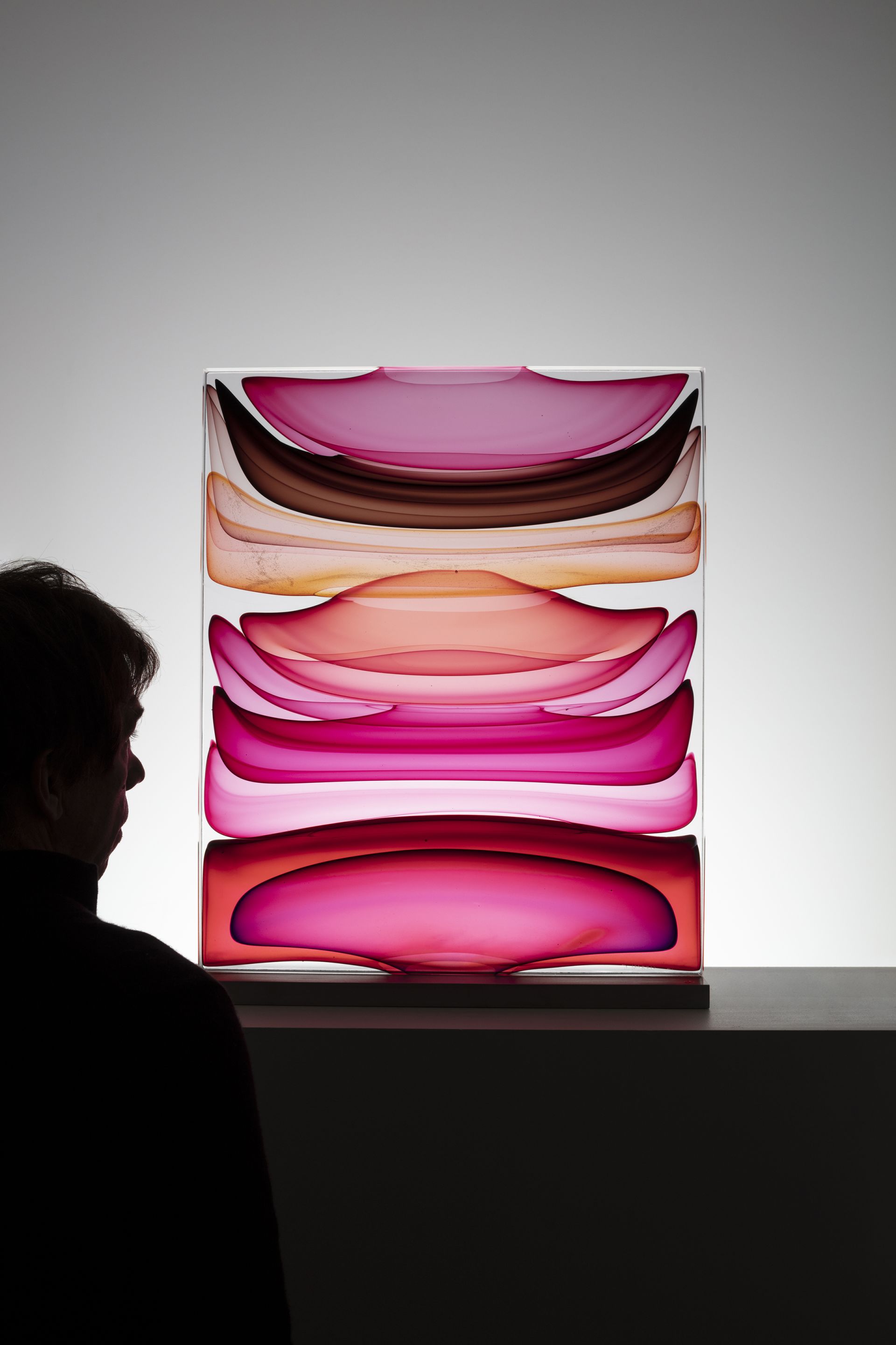 A man stands next to a handblown glass sculpture in rose, red, and orangey tones.