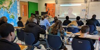 Kids in classroom listen to and watch Jonathan Spike (@Mr_JSpike), professor of Game Design and Learning at the University of Wisconsin via telecommunication