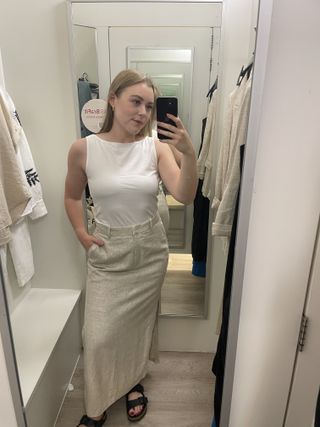 Woman in dressing room wears white vest and linen maxi skirt