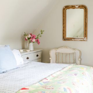 cottage bedroom with vintage mirror on wall, vase of roses on bedside drawers and vintage bed covers