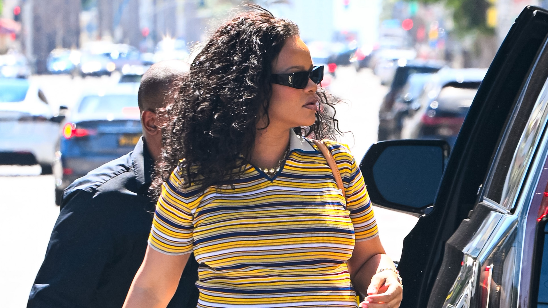 Rihanna styled ripped light-wash jeans with a striped polo shirt and a Louis Vuitton bag