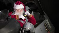 a man with a white beard in a red-and-white fur-lined suit straps himself into a fighter jet cockpit