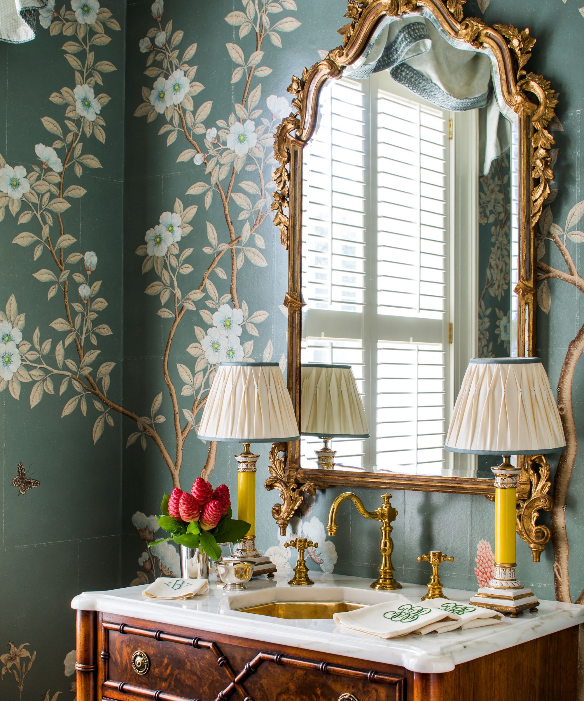 A wallpapered powder room with a wooden vanity topped with two lamps