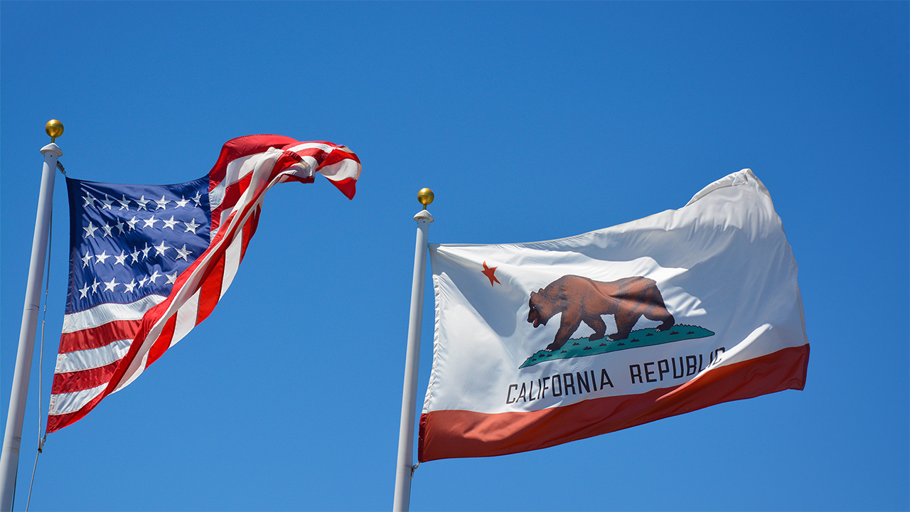 Flags of the US and California flying against a clear blue sky