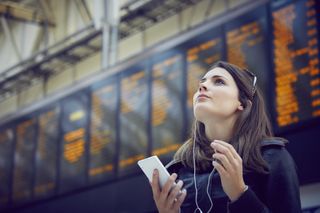 Woman at the airport looking at phone and wearing headphones