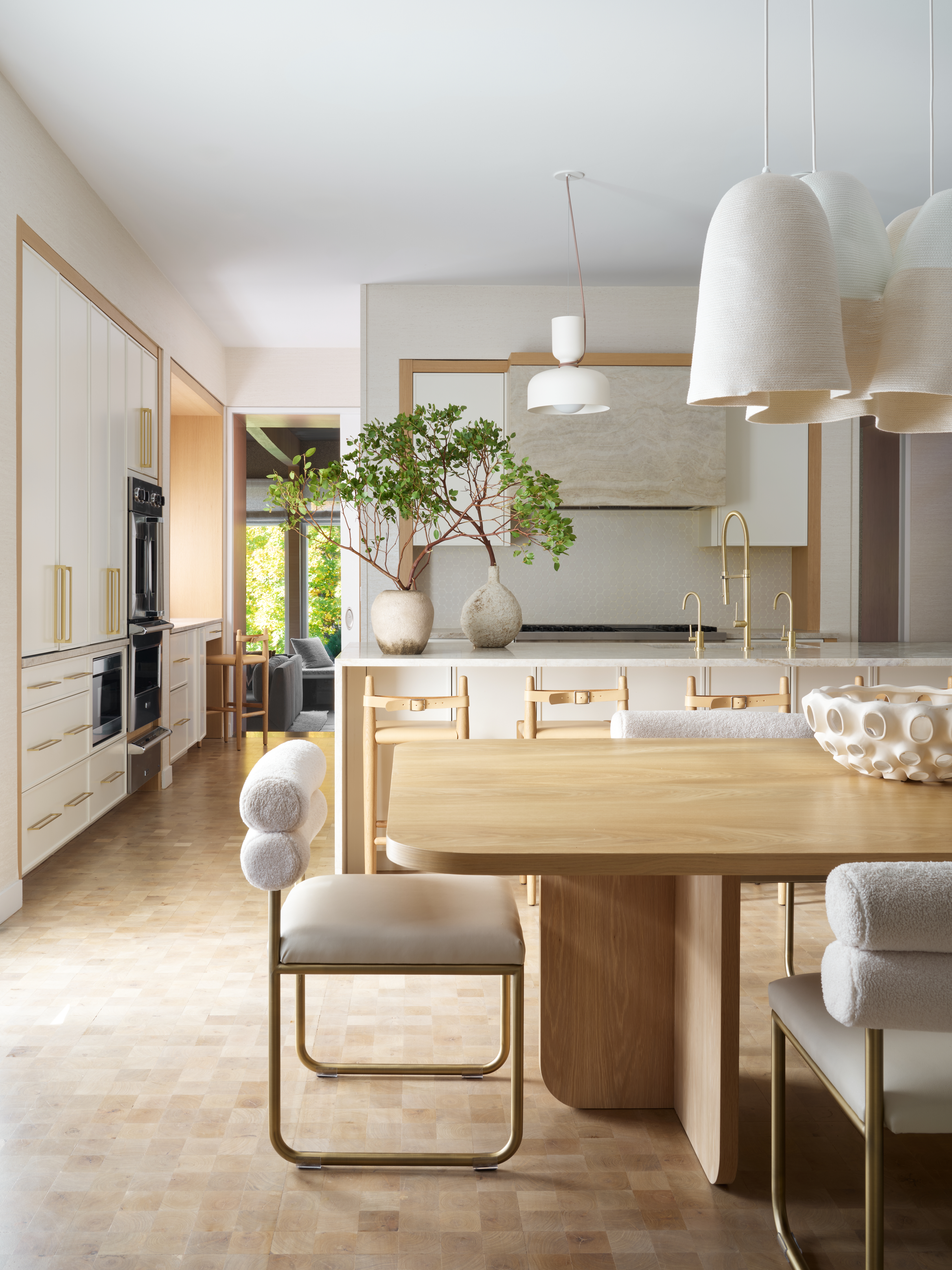 large modern kitchen with white cabinetry and gold accents, with counter seating at the island and a large dining table behind