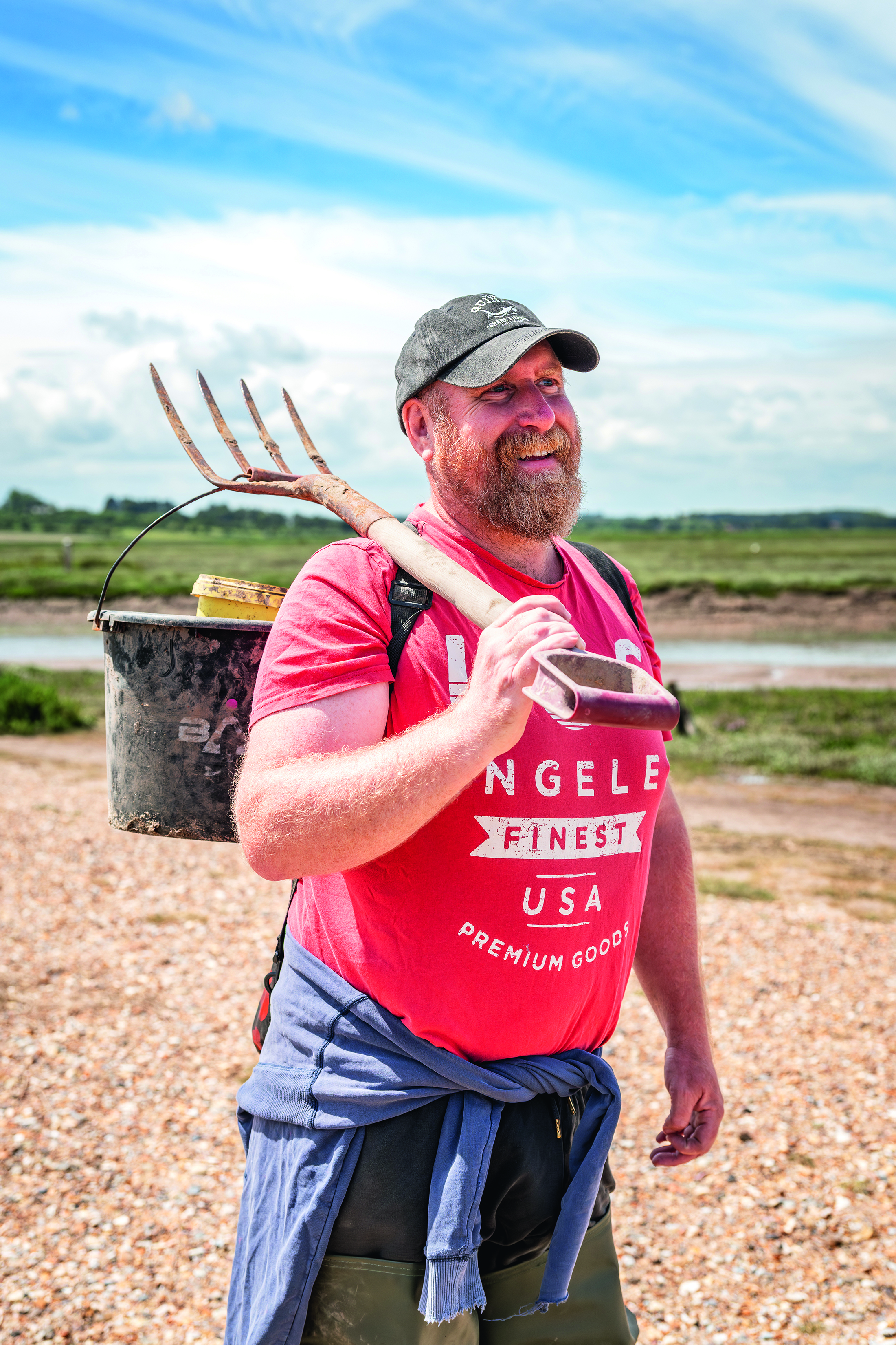 Bait digger Will holding a pitchfork and a bucket on the foreshore