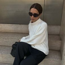 A woman wearing a white sweater and black pants