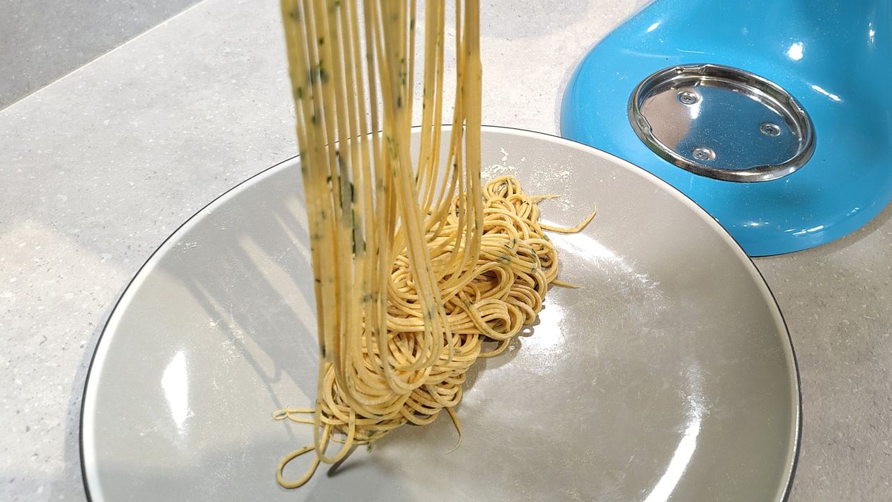 KitchenAid stand mixer with pasta roller attachment cutting tomato and basil spaghetti