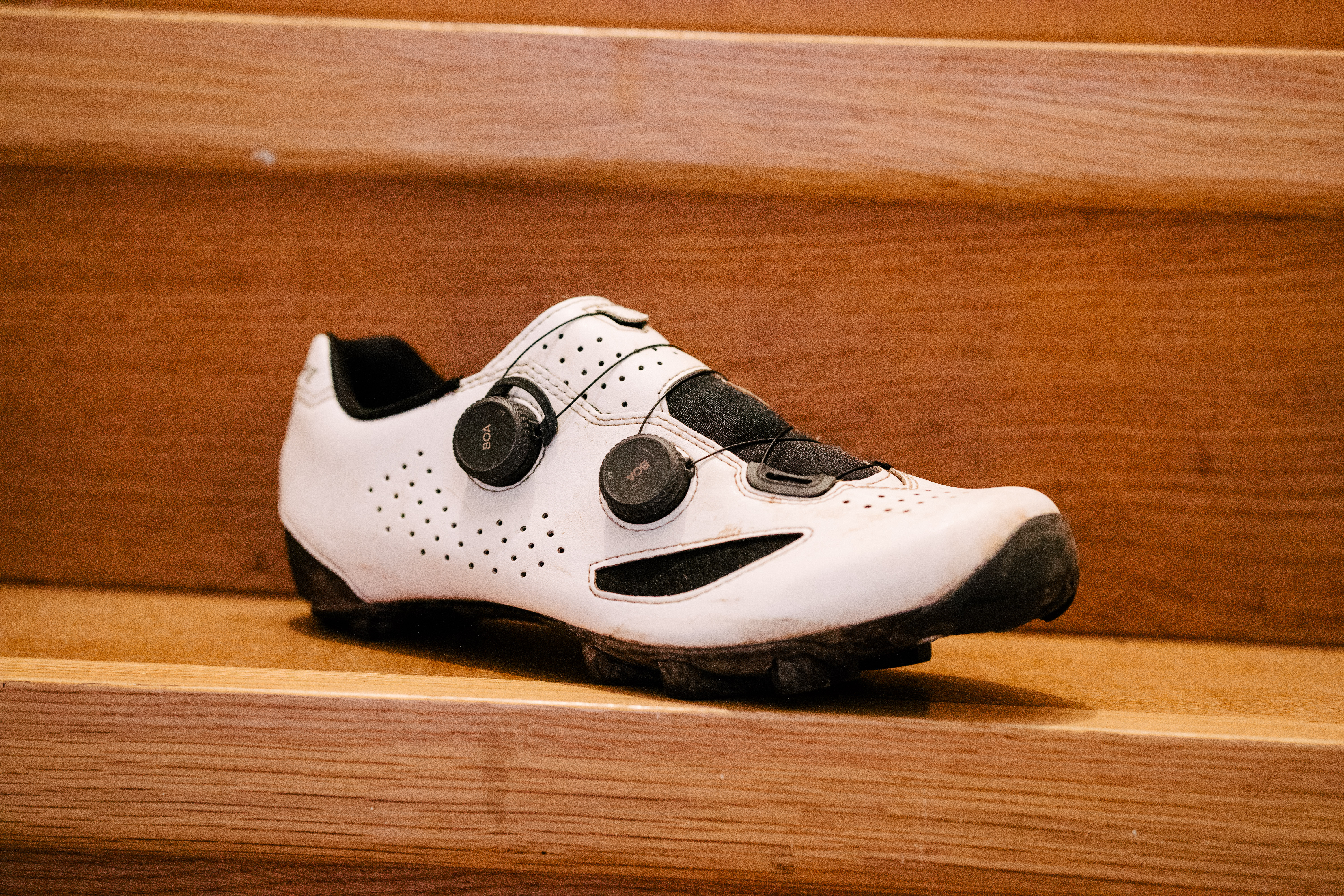 A white gravel bike shoe on wooden stairs