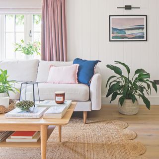 White living room with wooden floors and a jute rug, with a white sofa and coffee table on top of it