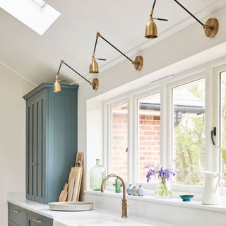 green and white kitchen with brass wall lights over kitchen sink