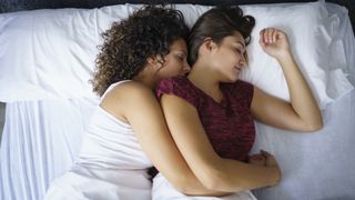 Two women sleep on their sides while cuddling in bed