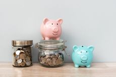 pink and blue piggy banks on wood table next to jars of coins