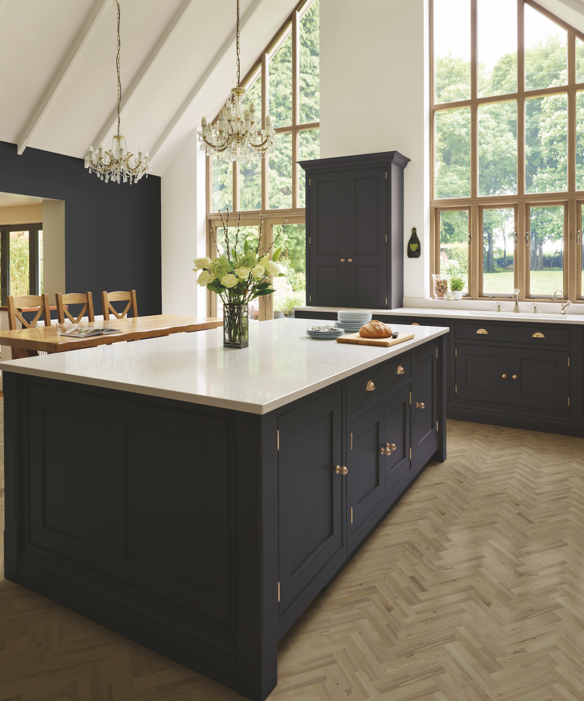 Navy blue kitchen color ideas with painted cabinetry, gold handles, chandelier lighting and wooden floor.